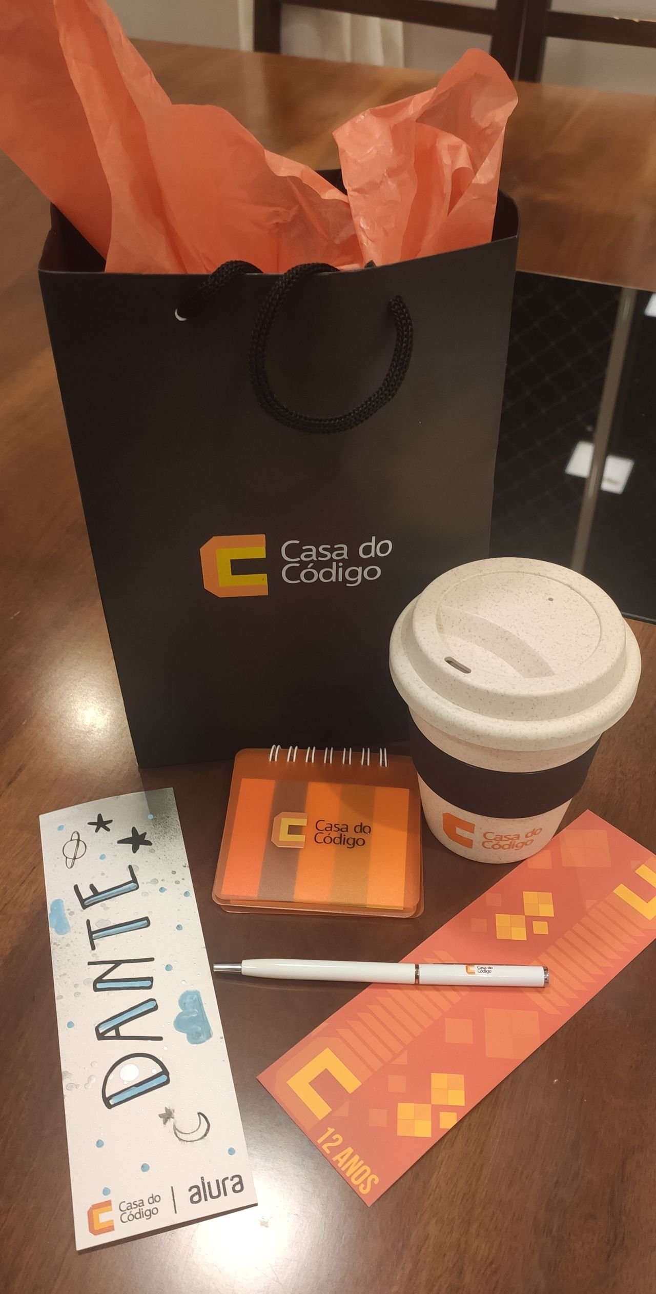 Bag, coffee cup, pad with post-its, pen and bookmark from Casa do Code; and another personalized bookmark (which says "Dante")